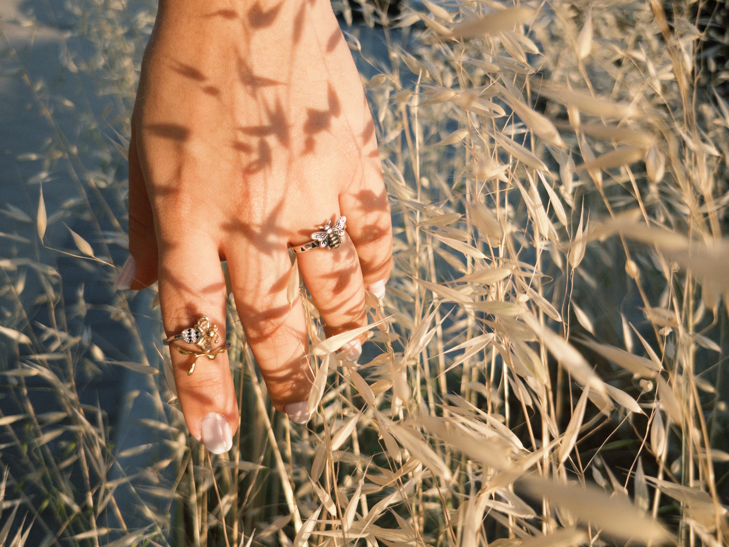 Anillos ajustables con diseño de abeja sobre una mano entre espigas doradas, colección de accesorios MielconmiGOD.
